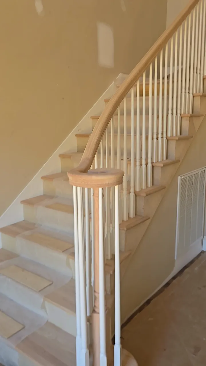 Wood handrail and white balusters following a staircase from curved lower steps to an upper landing